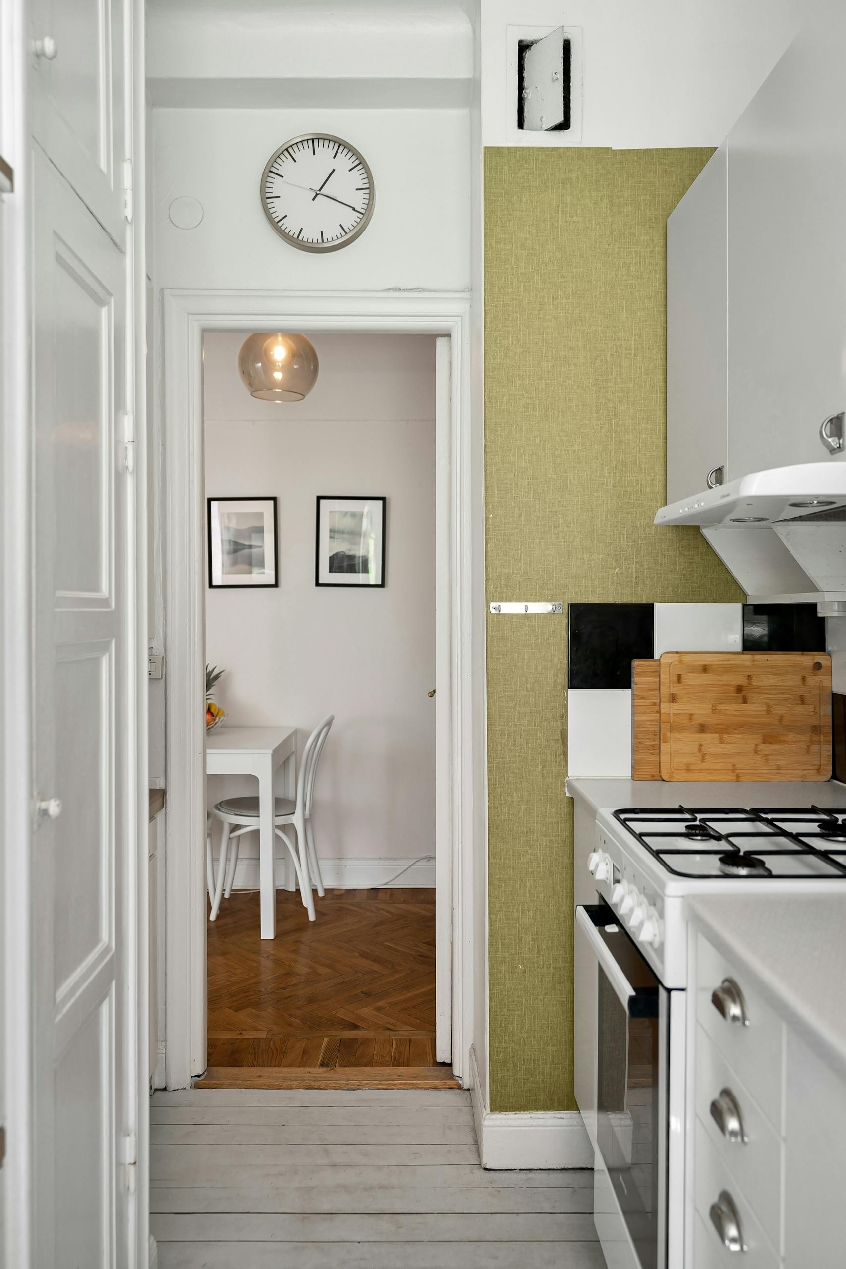 Contemporary narrow kitchen leading to a cozy dining area. Clean design with white and green accents.