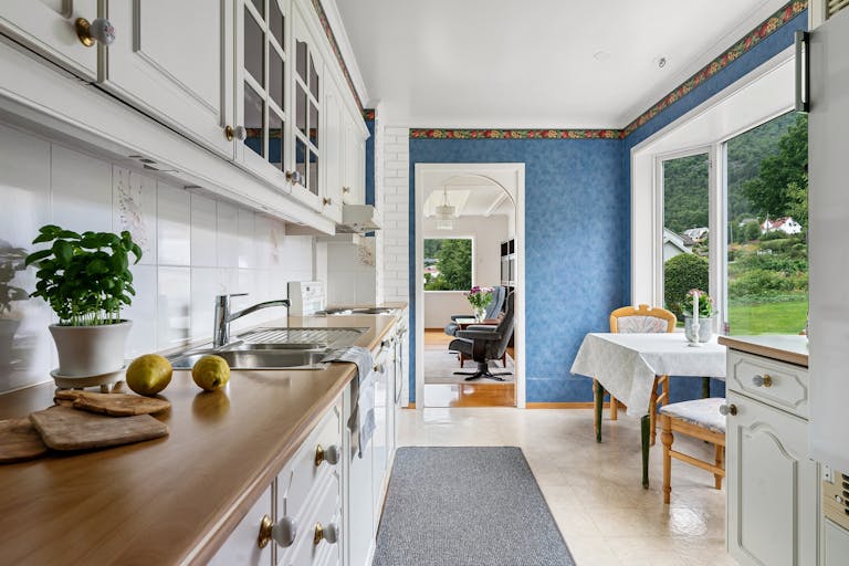 Spacious white kitchen with blue walls and natural light, featuring a dining area.