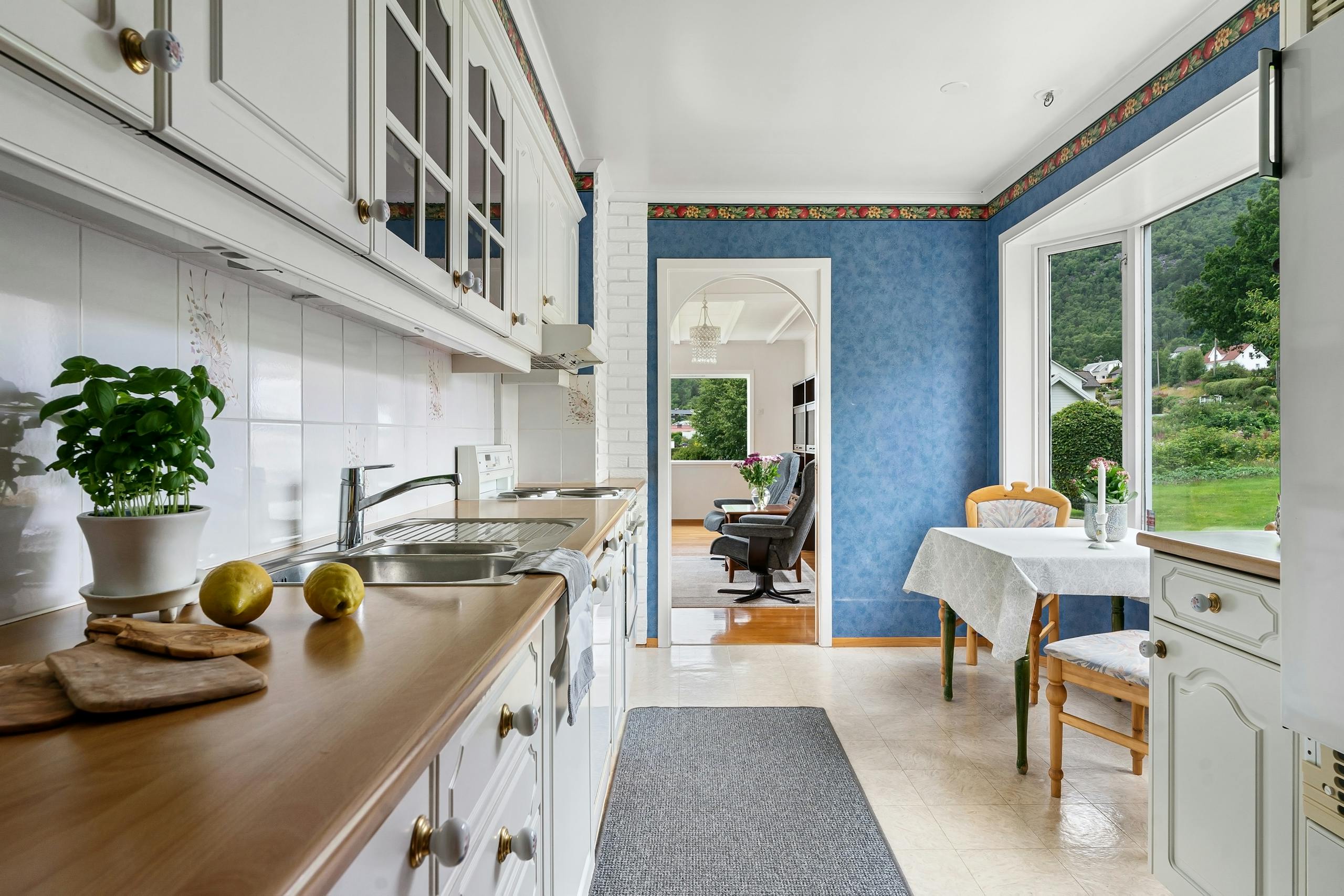 Spacious white kitchen with blue walls and natural light, featuring a dining area.